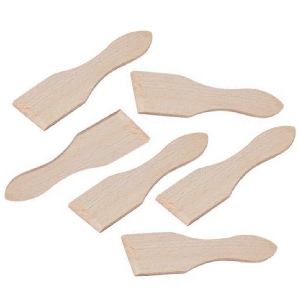 Six spatules en bois brun disposées près d’un appareil à raclette sur une table claire.