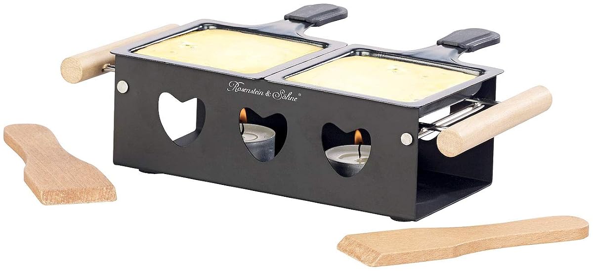 Appareil à raclette noir à bougies avec deux poêlons antiadhésifs et une spatule sur une table en bois.