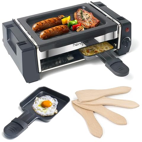 Mini appareil à raclette noir avec plancha, deux poêlons et spatules en bois sur une table